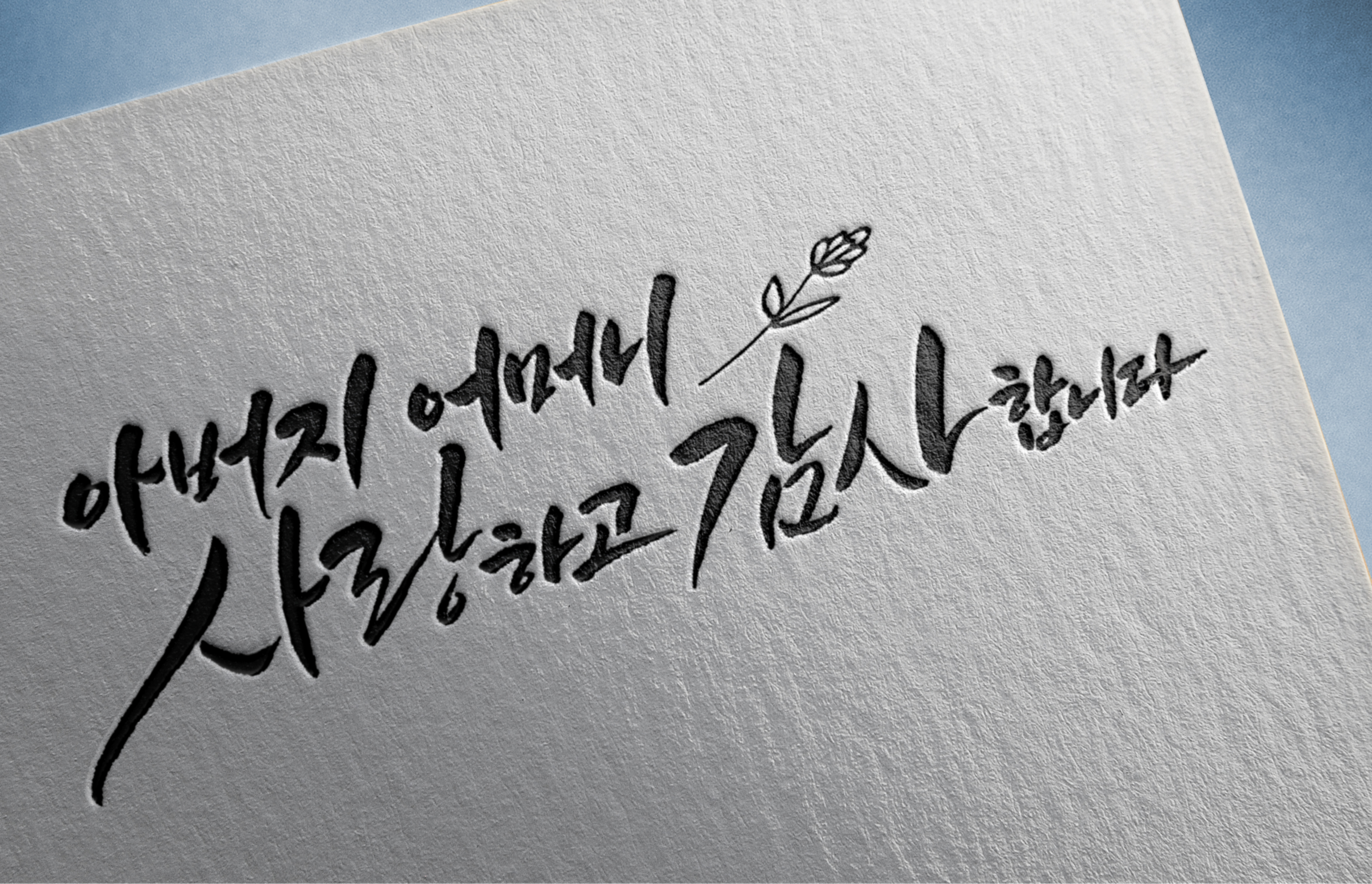 흰 종이 위에 검은색 붓글씨로 쓴 한국어 문구와 작은 꽃 그림이 보인다.