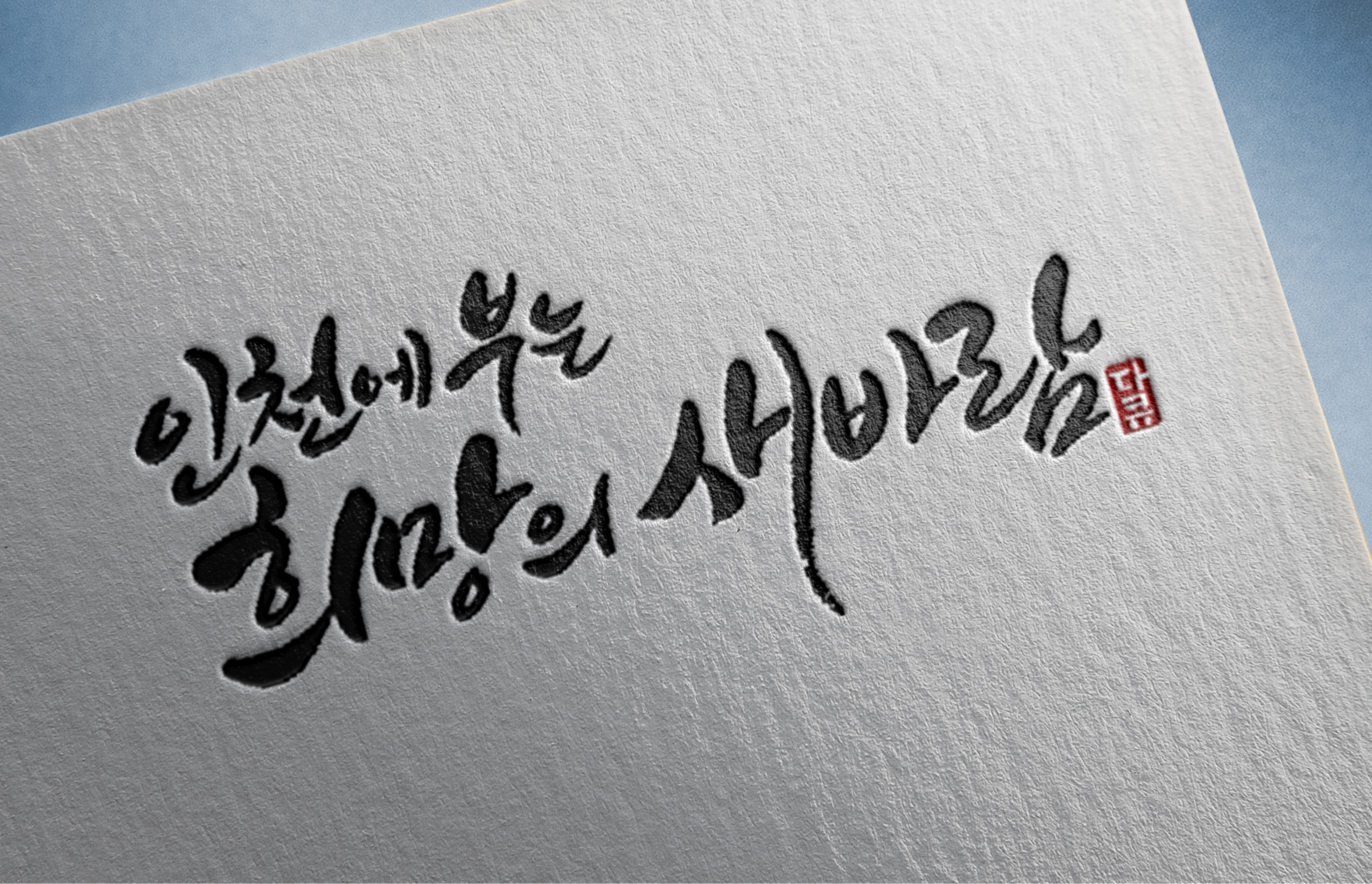 흰색 종이 위에 검은색 붓글씨로 쓴 한국어 문구가 대각선으로 인쇄되어 있다.